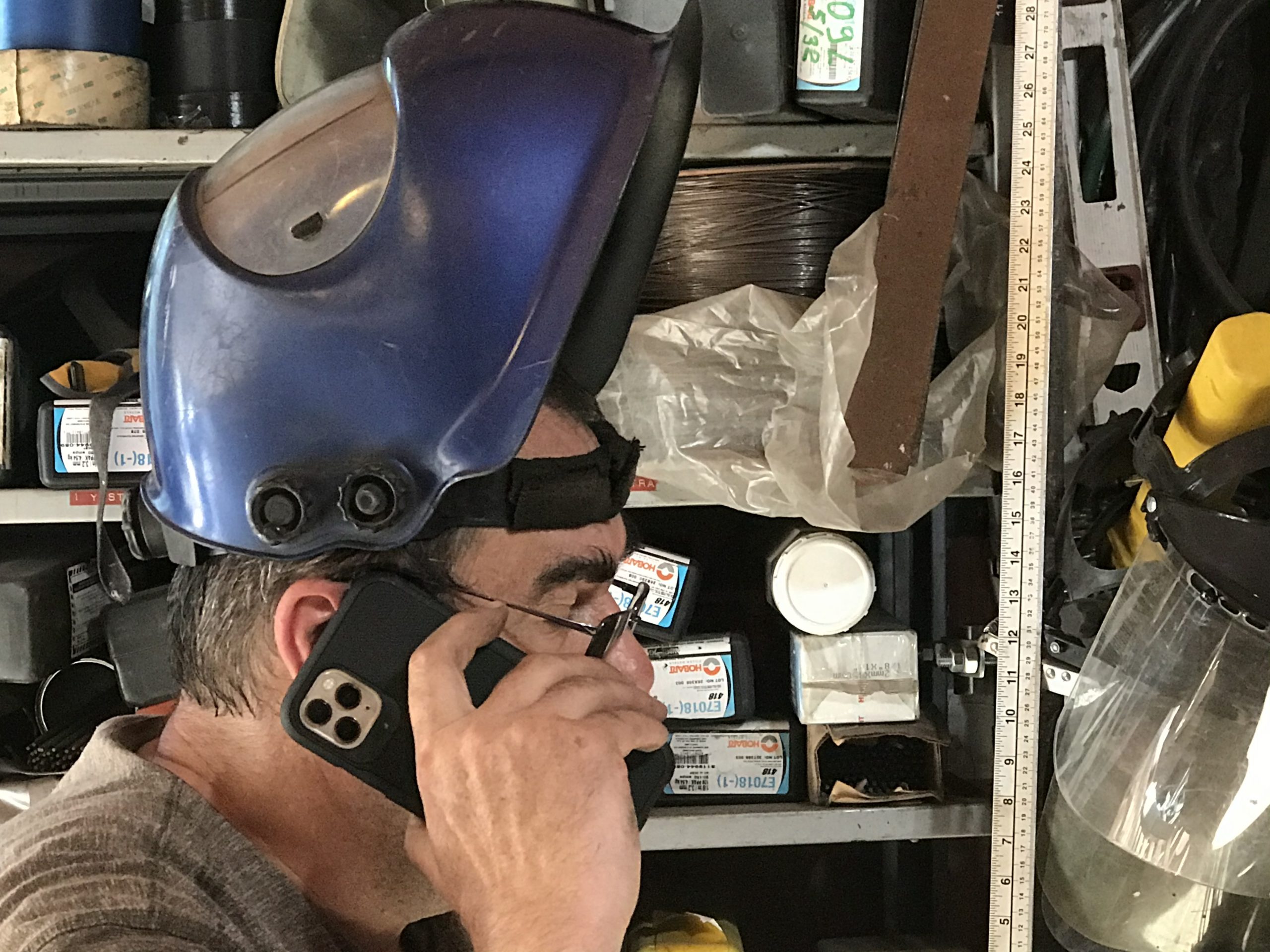 Welder in London Ontario , wearing a welding helmet, owner of JW Portable Welding & Repairs is talking to client on the phone