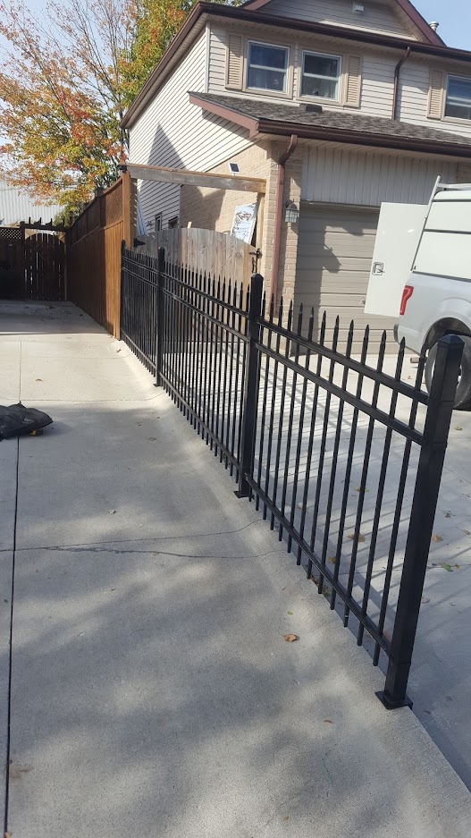 Medium height iron fence placed as extension of wooden fence. Fence's top prongs are sharpened. JW Portable Welding & Repair 2019 London Ontario