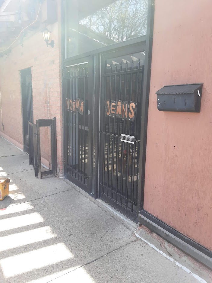 Side view of security grills with the sign Norma Jeans on bar's door with the glass panel. JW Portable Welding & Repairs 2019, London, Ontario