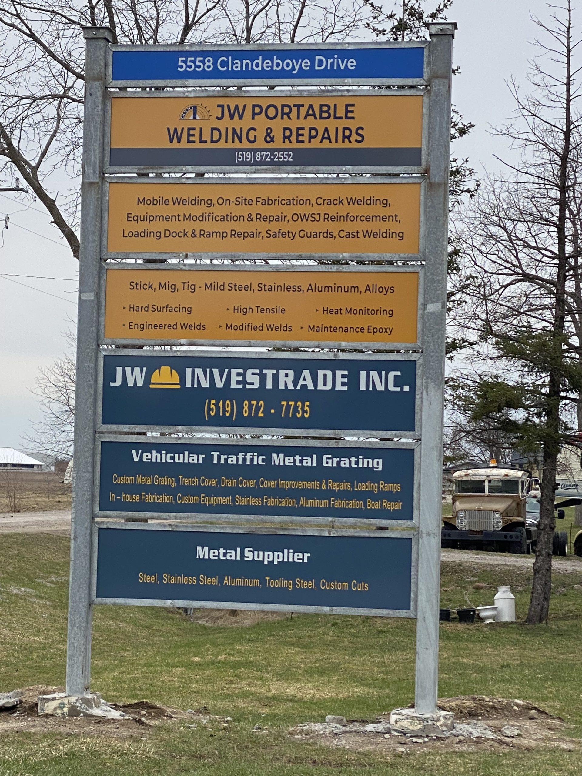 Exterior sign for two businesses containing the address, logos phone numbers, services and products. The steel structure of the sign is galvanized. JW Portable Welding & Repairs, Lucan Ontario, April 4, 2025