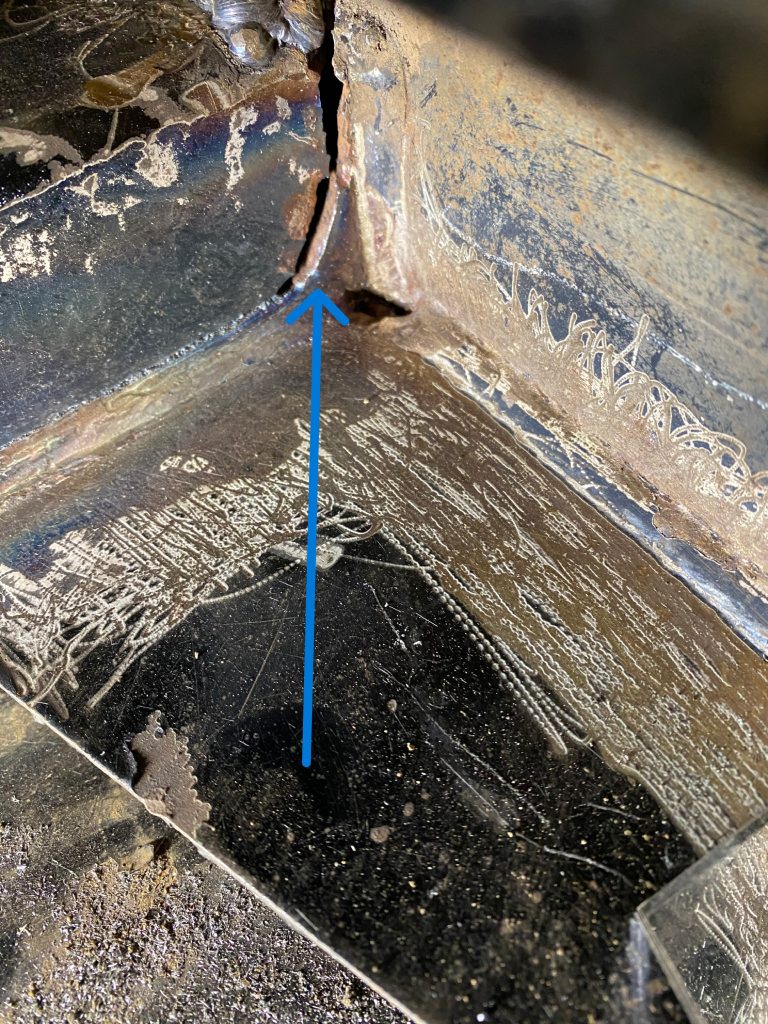 Cracked frame of this heavy equipment repair is a major issue. The blue arrow points to the crack. JW Portable Welding, London Ontario, May 2, 2023