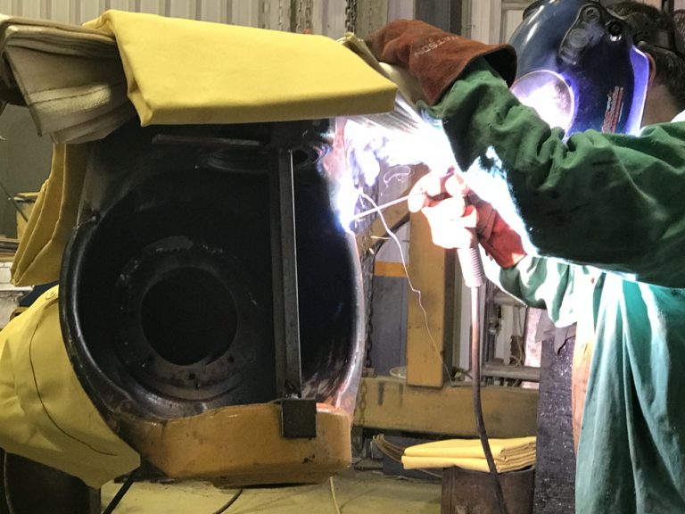 Large steel cast from the heavy transportation equipment is being welded by portable welder using SMAW technology. The welder holds the welding gun with a welding rod while welding this cast. JW Portable Welding, London, Ontario, 2018