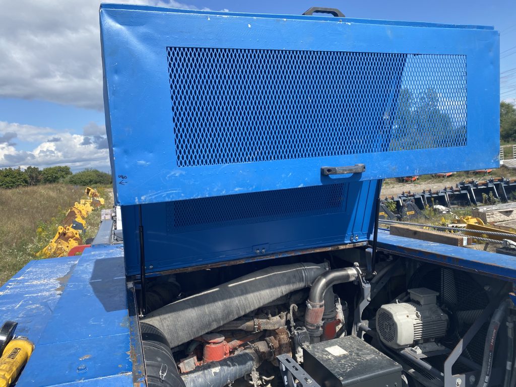 The front sectional engine cover of this machine is in open position and it is supported by two lifters. The lifters are in black color. The lifters allow to lift the whole sectional cover with just one hand.