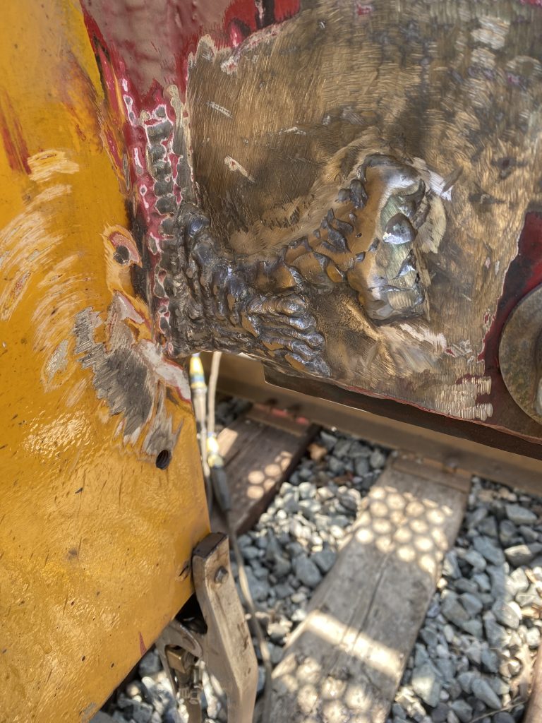 This is outside view of the welded crack in the locomotive bumper. This weld in the picture consist of two layers of large welds. First the bottom large multi-pass weld has followed the grooving and strengthened the bore wall. The second L shape multi- pass weld strengthen the edge were the crack has began by joining a large vertical weld and 2 inch bumper rim that is positioned inside. London ON, 2024, JW Portable Welding & Repairs.