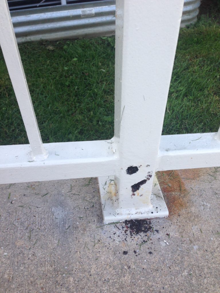 Steel post damaged by rust at the bottom. The rust is bulging through the white paint. The chipping hammer hit at the bottom of the post reveals the damaged by rust structure. Inspected by JW Portable Welding & Repairs 2019 London, Ontario