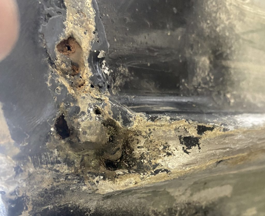 Holes in hull of the fishing aluminum boat near stern caused by dragging the boat on the stones. The image prior cleaning and welding. Dragging the boat on the shore's stones causes holes in the hull. For JW Portable Welding, Lucan, 2025